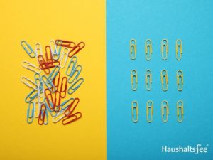 Das Bild zeigt eine Gruppe von bunten Büroklammern, die auf einem Holztisch liegen. Die Büroklammern sind in verschiedenen Farben, darunter Rot, Blau, Grün und Gelb. Der Hintergrund ist verschwommen und unscharf, was darauf hinweist, dass der Fokus des Bildes auf den Büroklammern liegt.